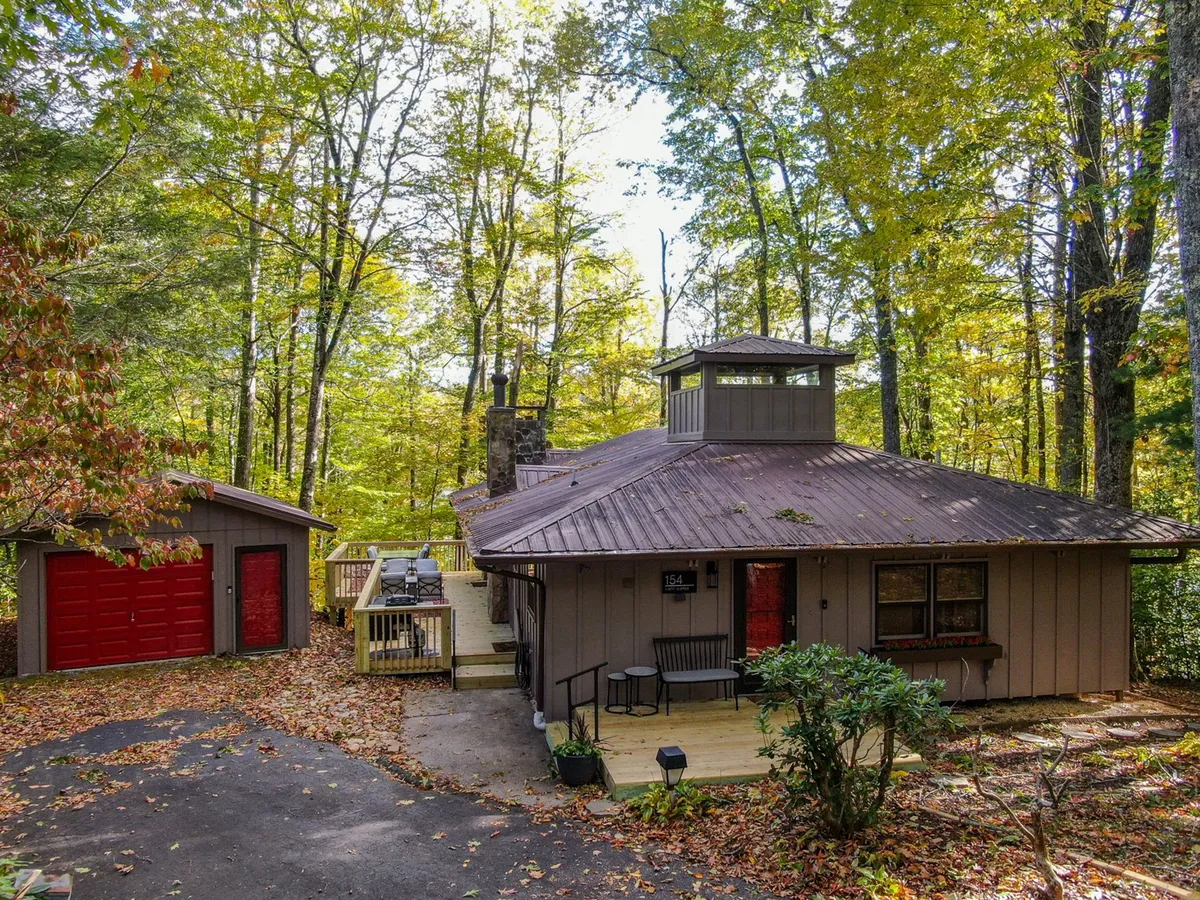 This exterior shot highlights the unique architectural design of the property, featuring red garage doors, a wooden deck with comfortable seating, and a backdrop of lush trees. The inviting deck space suggests a welcoming spot for outdoor gatherings and relaxation after a day of exploration.