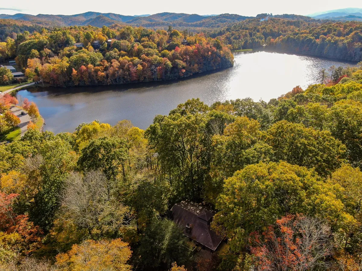 This image features a serene lake surrounded by vibrant autumn foliage, with mountains rising in the distance and houses nestled along the shoreline. The calm water reflects the colorful leaves, creating a tranquil and picturesque setting that captures the essence of outdoor adventure and natural beauty.