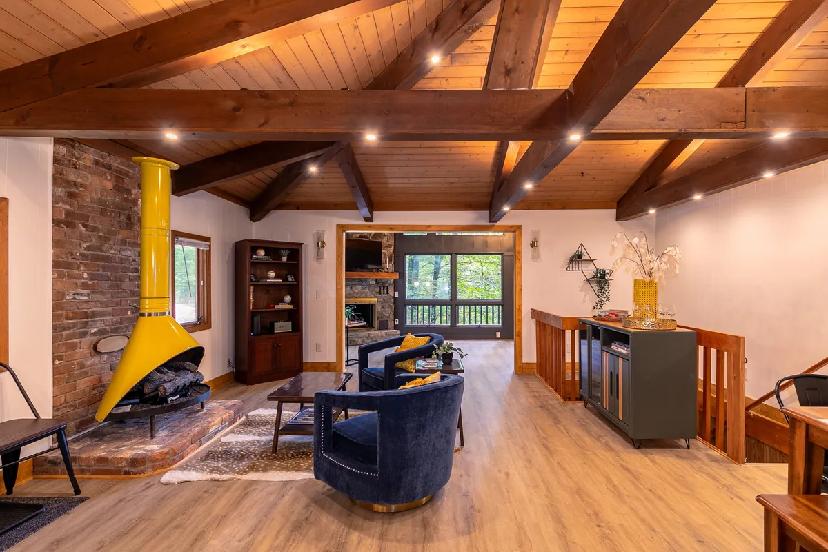A cozy, inviting recreation room with a bold yellow fireplace, blue chairs, wooden beams, and a stone wall. The space is alive with warmth and comfort, ideal for socializing, reading, or relaxing by the fire, and offers a glimpse of communal indoor amenities available to residents during the season.