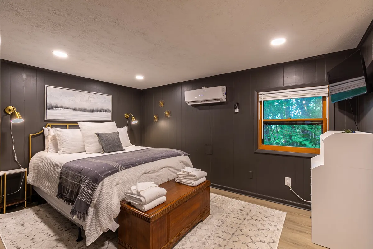 A tranquil bedroom featuring a comfortable bed positioned near a window, with calming artwork and nightstands flanking the bed. Soft natural light fills the room, highlighting its peaceful ambiance—perfect for rest and relaxation.