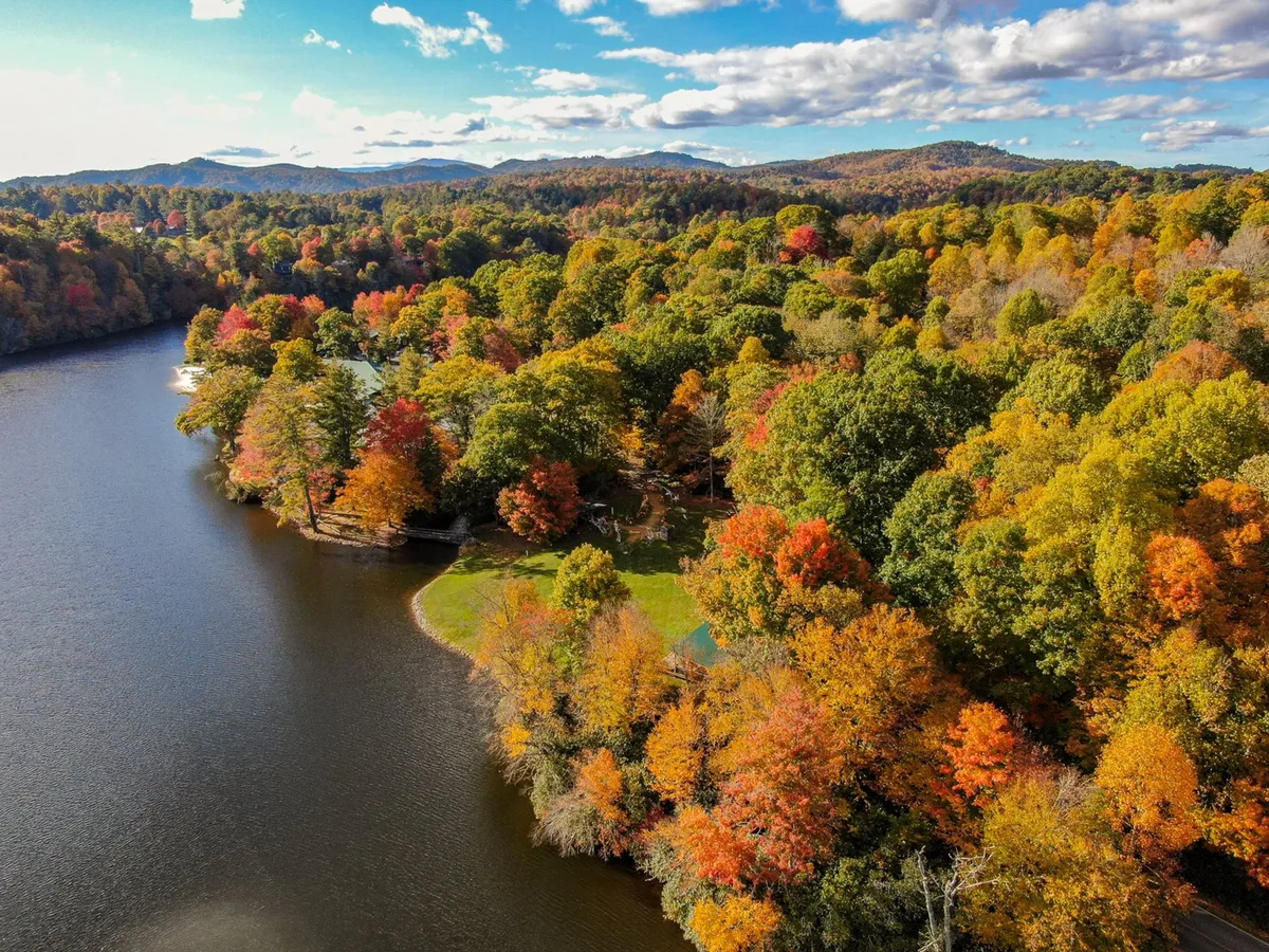 This sweeping view captures colorful autumn foliage around a calm lake, with distant mountains and green spaces on the shoreline. The setting is ideal for hiking, boating, fishing, and family picnics, evoking a sense of exploration and seasonal beauty.
